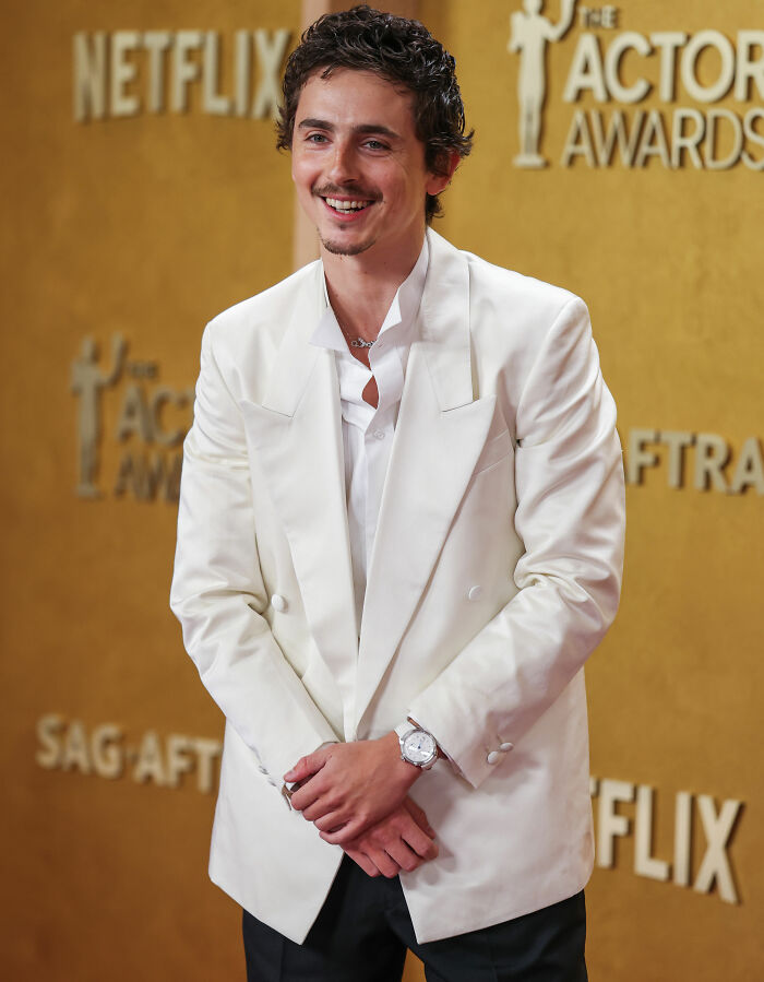 Timoth&eacute;e Chalamet smiling in a white suit at the Actor Awards, sparking fan theories about his date and presence.