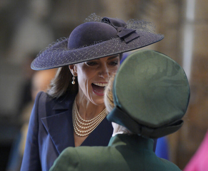 Kate Middleton in a navy hat and pearl necklace speaking closely during a tense royal gathering with Prince William.