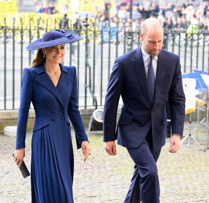 Prince William and Kate Middleton dressed in navy blue attire attending a formal royal gathering outdoors.