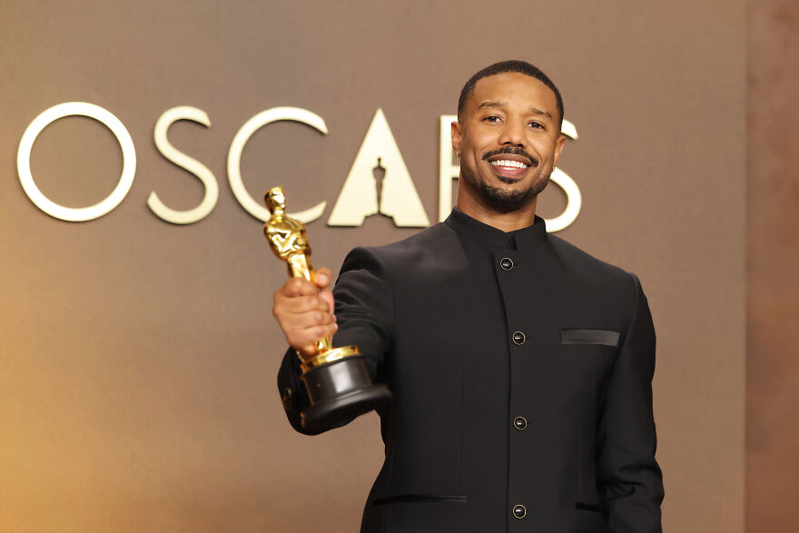Michael B. Jordan holding Oscar statue, smiling confidently after historic Best Actor win at the Oscars event.