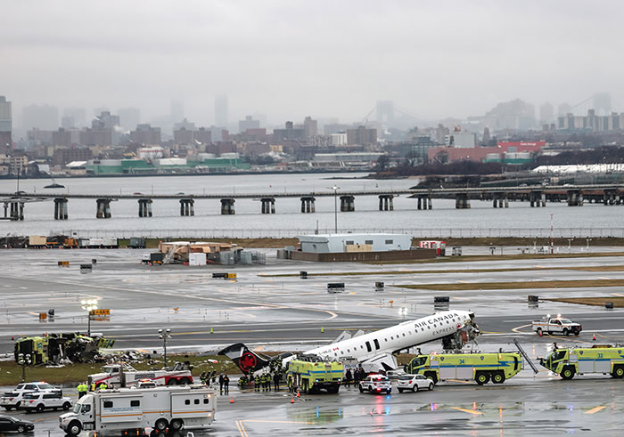 Cena de resgate de comissário de bordo da Air Canada no aeroporto LaGuardia após acidente com veículos de emergência e bombeiros em pista molhada.