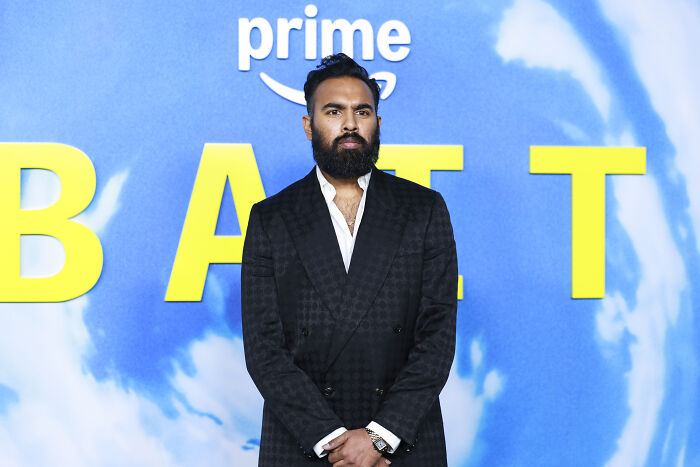 Man with a beard and dark suit standing in front of a blue backdrop at an event related to Ryan Coogler's X-Files reboot.