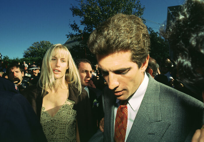Daryl Hannah and JFK Jr. interacting outdoors surrounded by people in a candid historical moment.