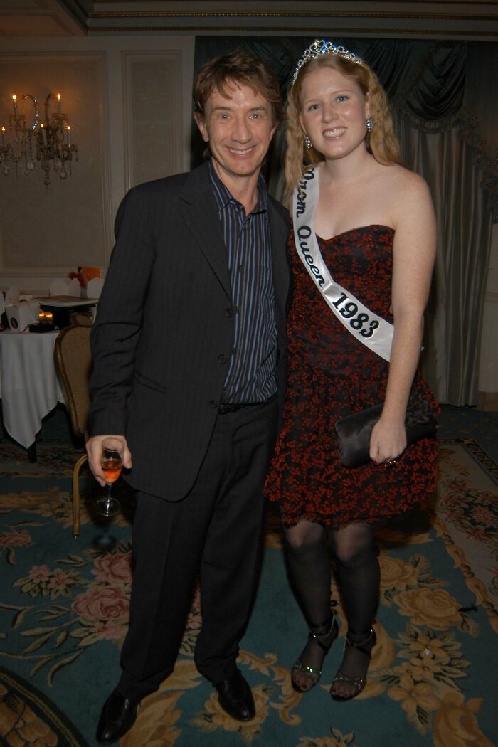Man in suit holding drink stands next to woman wearing prom queen sash and tiara at formal indoor event discussing cause behind Katherine Short’s passing. Man in suit holding drink stands next to woman wearing prom queen sash and tiara at formal indoor event discussing cause behind Katherine Short’s passing.
