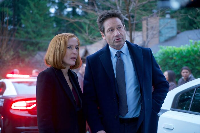 Actors in Ryan Coogler's X-Files reboot scene, standing near police cars with flashing lights in outdoor setting.