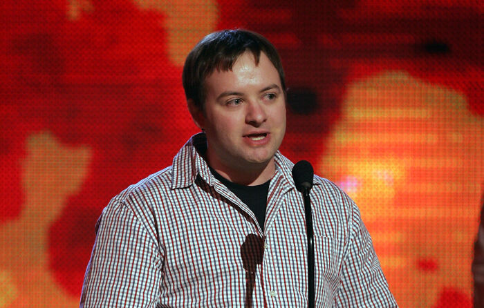 A man speaking into a microphone against a red background, related to God Of War creator slamming Amazon live-action.