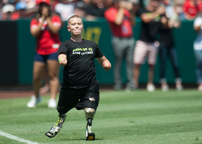 Man with no arms or legs running on a sports field with prosthetic limbs during an outdoor event.