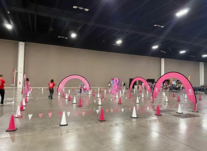 Indoor Barbie Dream Fest event space with pink cones and arches, featuring queuing areas and a few attendees walking around.