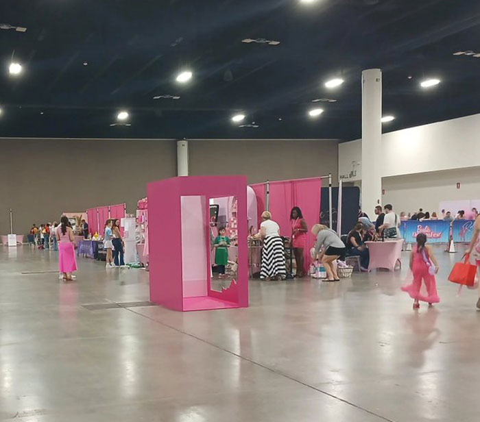 Attendees at Barbie Dream Fest walking and interacting near pink booths in a large indoor event space.
