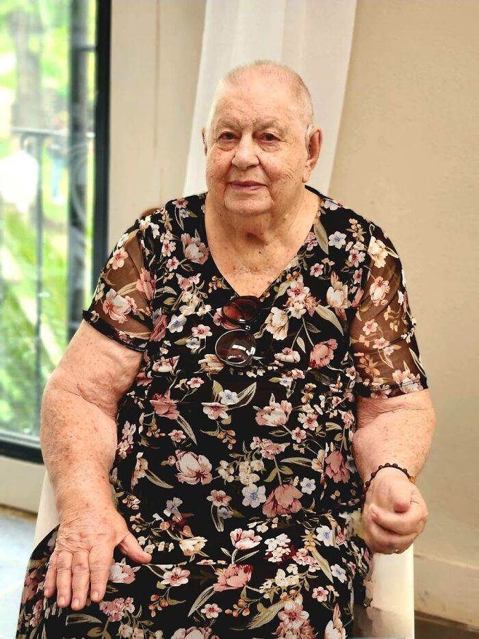Elderly woman in floral dress sitting indoors, reflecting on crazy things people did for love in the past.