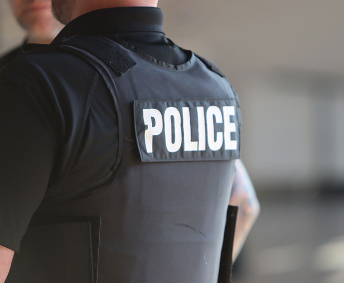 Policial vestindo um colete preto com etiqueta policial, parado em um ambiente interno, sem saber das preocupações com a embalagem da Barbie. Policial vestindo um colete preto com etiqueta policial, parado em um ambiente interno, sem saber das preocupações com a embalagem da Barbie.