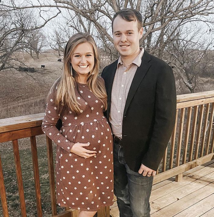 Joseph Duggar and his wife smiling outdoors on a wooden deck with bare trees in the background.