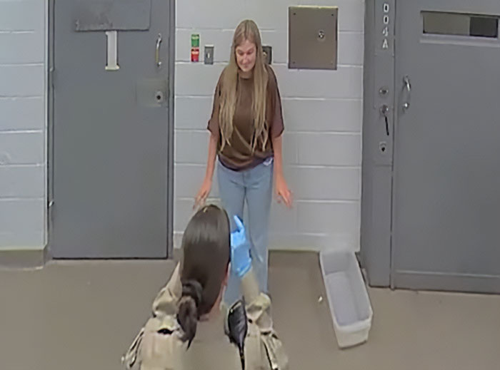 Woman in casual clothes standing in a room while neighbor reacts amid wife&rsquo;s arrest in Duggar family allegations.