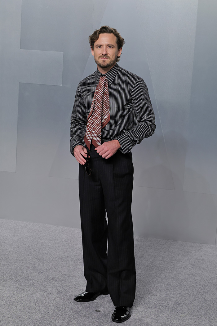 Man posing in pinstripe shirt and patterned tie, showcasing one of the biggest fashion fails at Oscars afterparties.