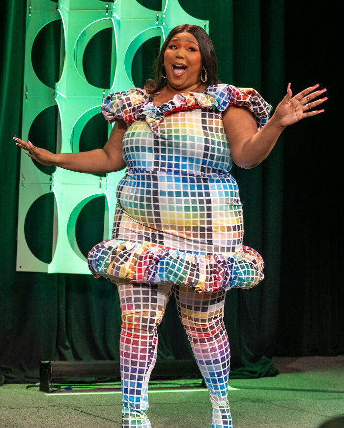 Plus-size woman in colorful grid-patterned outfit expressing excitement on stage, related to celebrities people now hate.