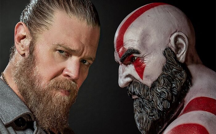 Man with beard staring intensely beside a detailed God of War character bust in a dark setting highlighting creator reaction to Amazon.