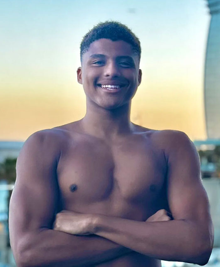 Young smiling athlete standing shirtless with arms crossed, related to bombshell claims of underwater incident and Hollywood connection.