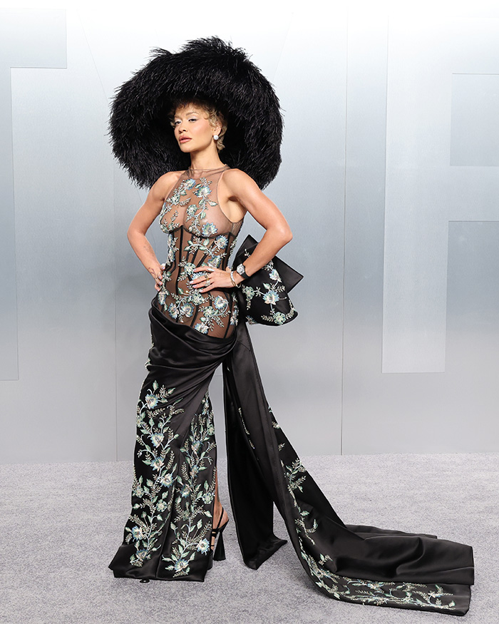 Woman in a floral embroidered sheer gown and oversized black feathered hat showcasing fashion fails at Oscars afterparties.