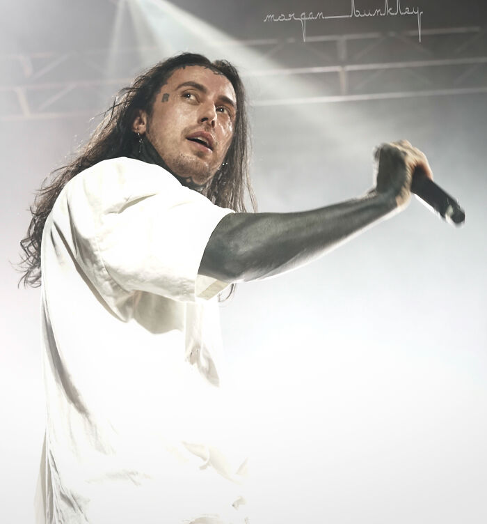 Male celebrity with long hair performing on stage, holding microphone, expressing intense emotion during live concert event.