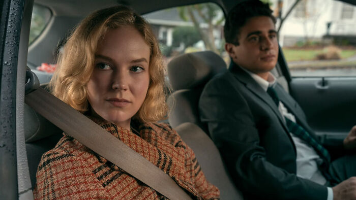 Young Scarpetta actress on Prime sitting in a car wearing a plaid coat, sharing role with Nicole Kidman.