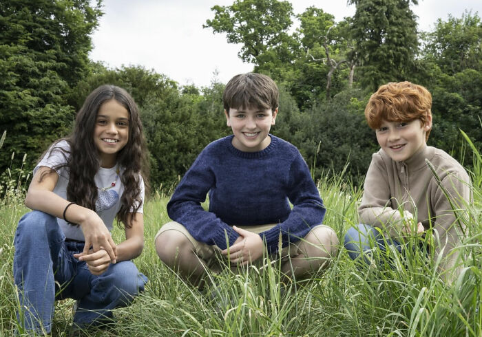 Three children sitting in a grassy field with trees behind, illustrating new name tops list to play Voldemort concept. Three children sitting in a grassy field with trees behind, illustrating new name tops list to play Voldemort concept.
