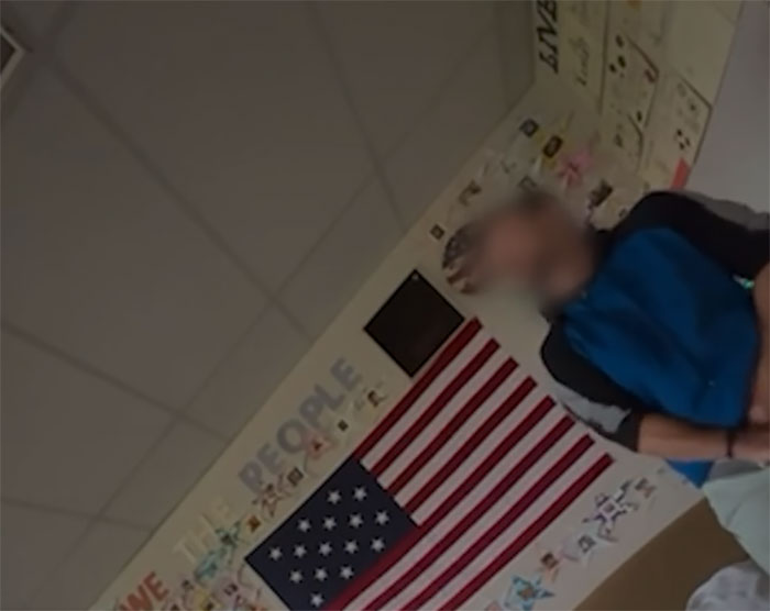 Blurred California teacher in classroom near American flag during bizarre act secretly filmed by student.