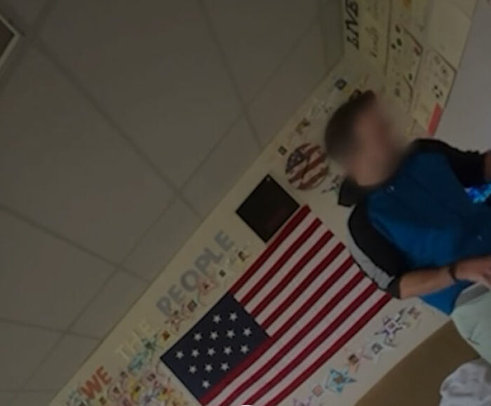 California teacher in classroom with American flag and student-made posters, blurred face to protect identity.
