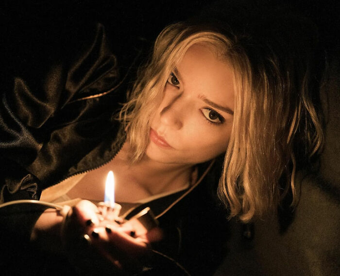 Anya Taylor-Joy in dim light holding a lighter, her latest interview appearance sparking heated debate among fans.