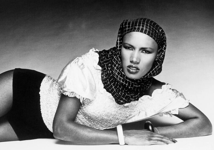 Black and white portrait of a woman wearing a checkered headscarf, posing confidently in stylish clothing.
