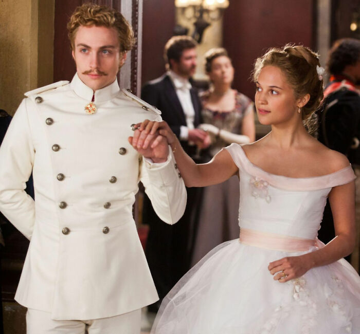 Aaron Taylor-Johnson in period costume holding hands with a woman in a white dress, showing evolved form changes. Aaron Taylor-Johnson in period costume holding hands with a woman in a white dress, showing evolved form changes.