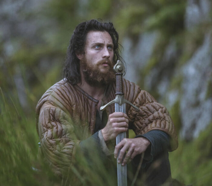 Man with long hair and beard holding a sword outdoors, showing an evolved form of Chalamet with noticeable appearance changes. Man with long hair and beard holding a sword outdoors, showing an evolved form of Chalamet with noticeable appearance changes.