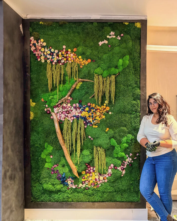 Woman standing next to a large green wall art with colorful flowers and branches, showcasing a DIY win and creative healing project.