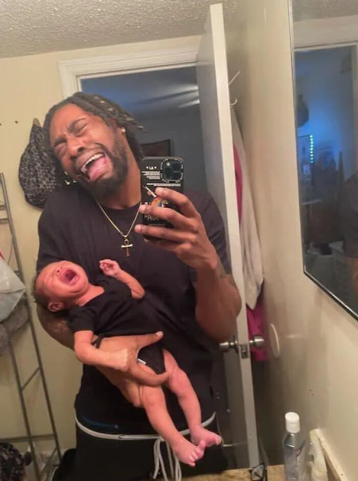 Man holding a crying baby while making a funny face, showcasing one of the creative poses people pulled off perfectly.