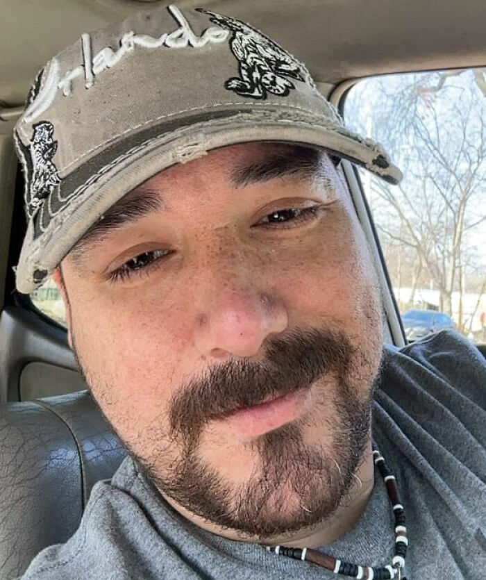 Man with a beard and cap inside a car, related to bodies of father and daughter found on gravel road story.