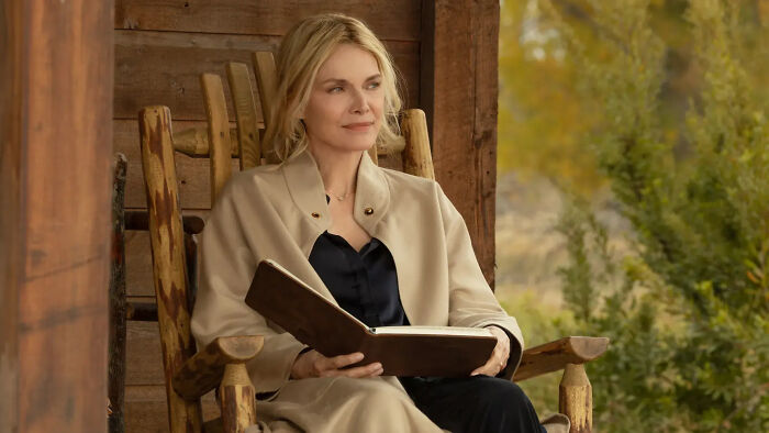 Woman sitting on a wooden porch chair, holding a book, representing Dutton Ranch release date for Yellowstone successor.