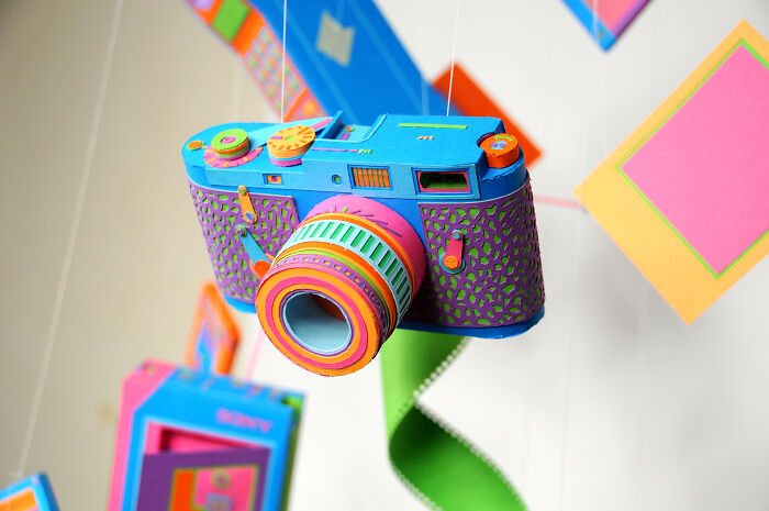 Colorful handcrafted paper camera created by French artist duo, showcasing intricate and vibrant paper art craftsmanship.