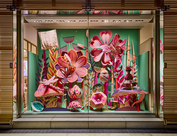 Intricate handcrafted paper art display by French artist duo featuring vibrant flowers and insects in a colorful window.