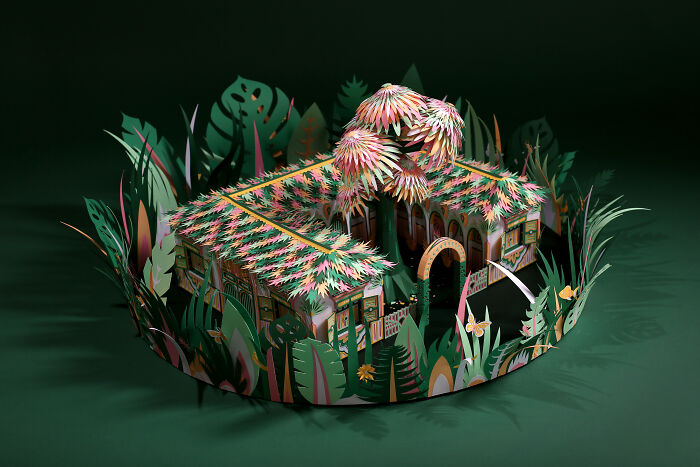 Intricate handcrafted paper model of a tropical hut surrounded by lush foliage, showcasing paper art by a French artist duo.