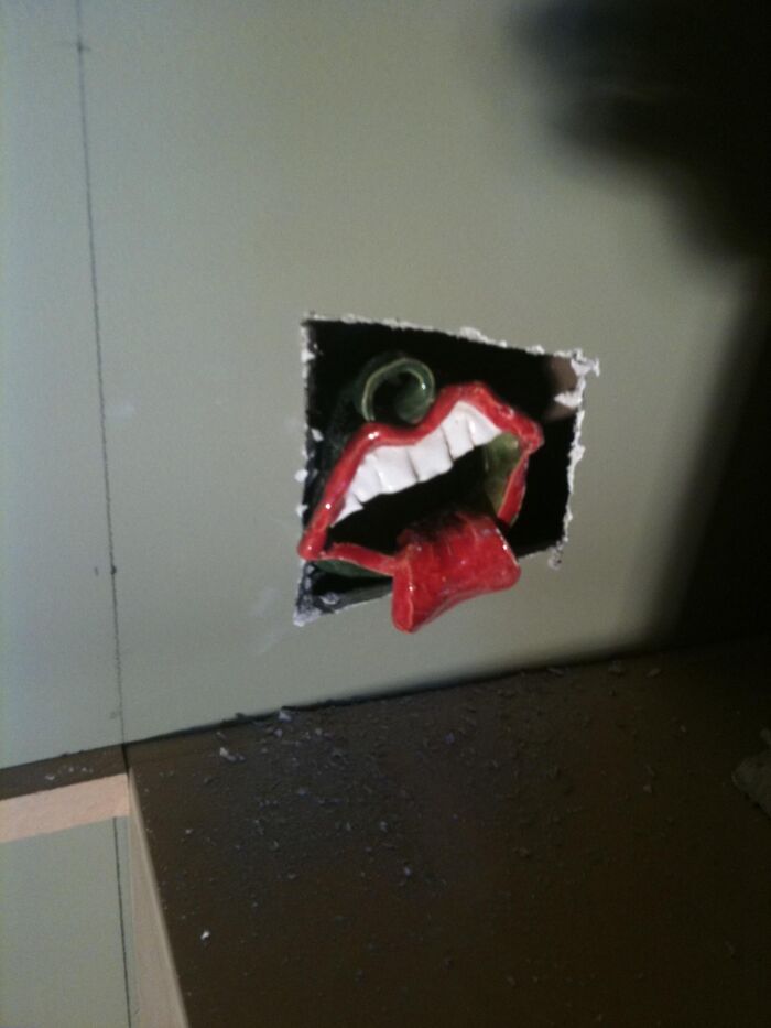 Red mouth with tongue sticking out installed in a wall hole, a weird and unhinged family tradition decoration.