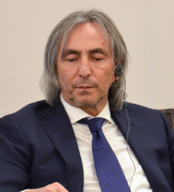 Politician wearing a suit and headset, looking down thoughtfully after Epstein files reveal his connection to Ghislaine Maxwell.