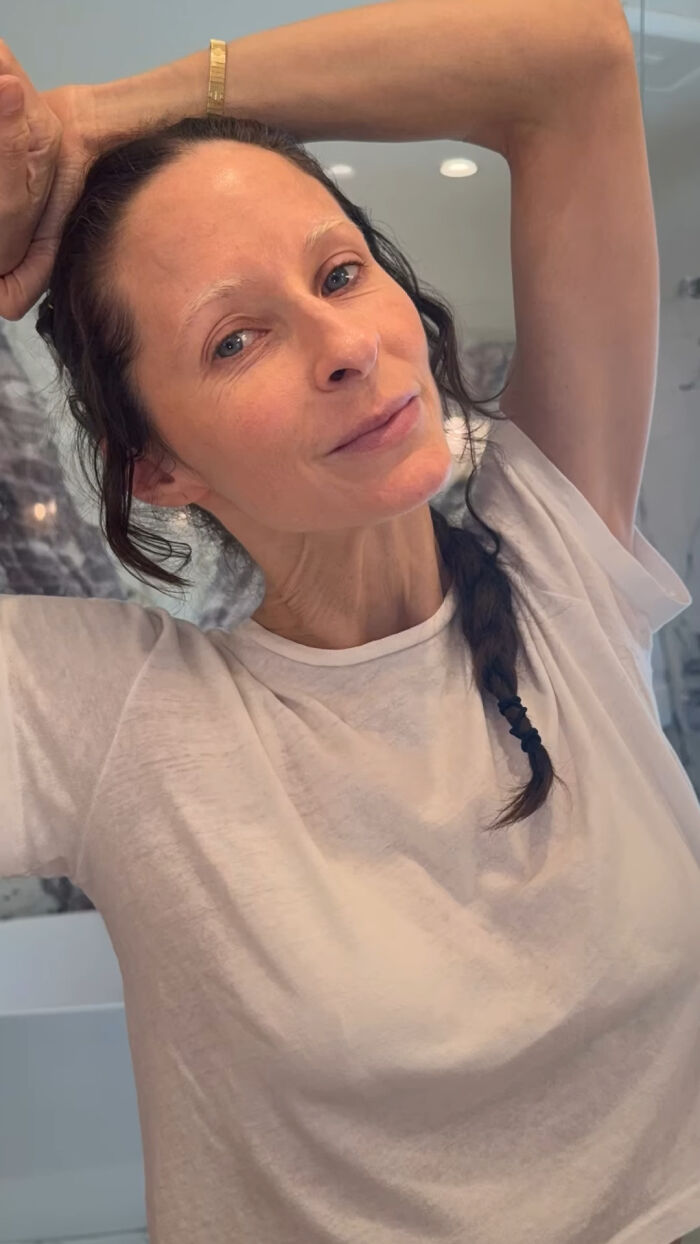 Emilie Goldblum in a white t-shirt with braided hair posing indoors, known for her pantsless look at Oscars afterparty.