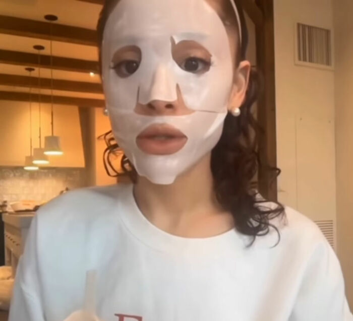 Woman wearing a white facial mask indoors, sparking Ariana Grande plastic surgery rumors after showing latest look.