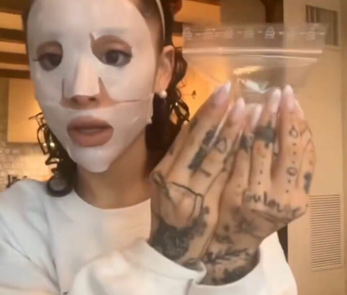 Ariana Grande wearing a white facial mask and showing her tattooed hands, sparking plastic surgery rumors with her latest look.
