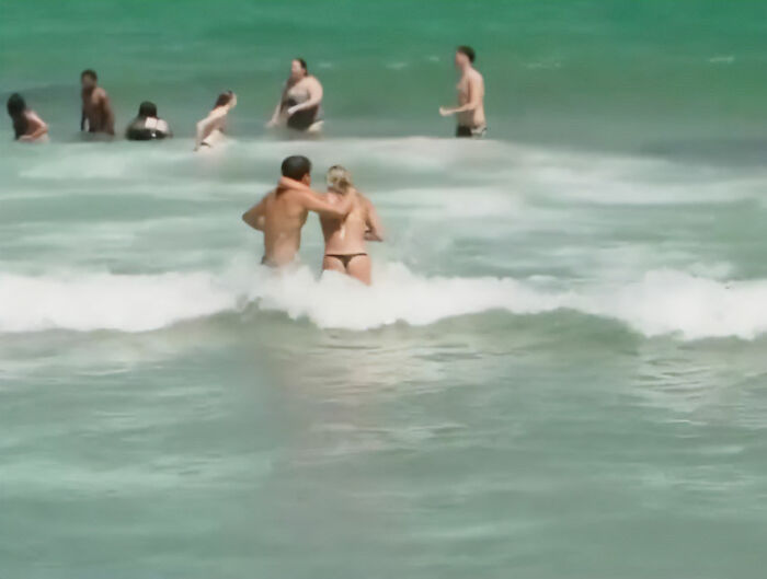 Crowd of spring breakers in swimsuits playing in ocean waves during viral video capturing vapid news answers.