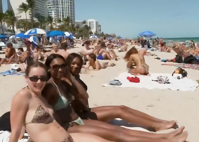 Group of spring breakers in swimsuits relaxing on a crowded beach during a sunny day in a viral video.