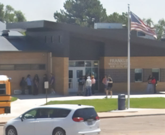 Exterior view of a middle school with people gathered outside, related to middle school secretary and disturbing crimes.