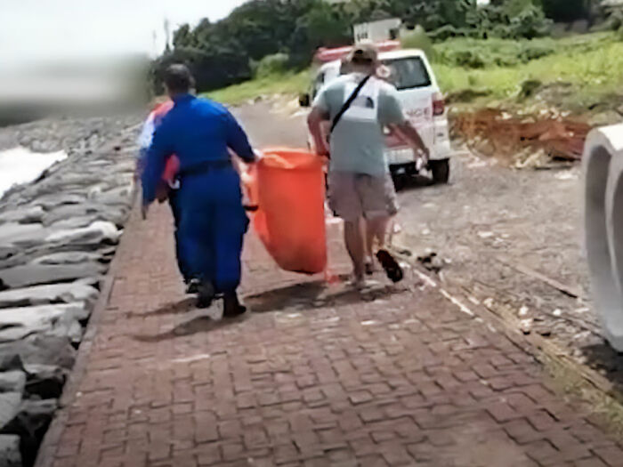 Police officers carrying an orange body bag along a coastal path after a disturbing discovery in Bali.