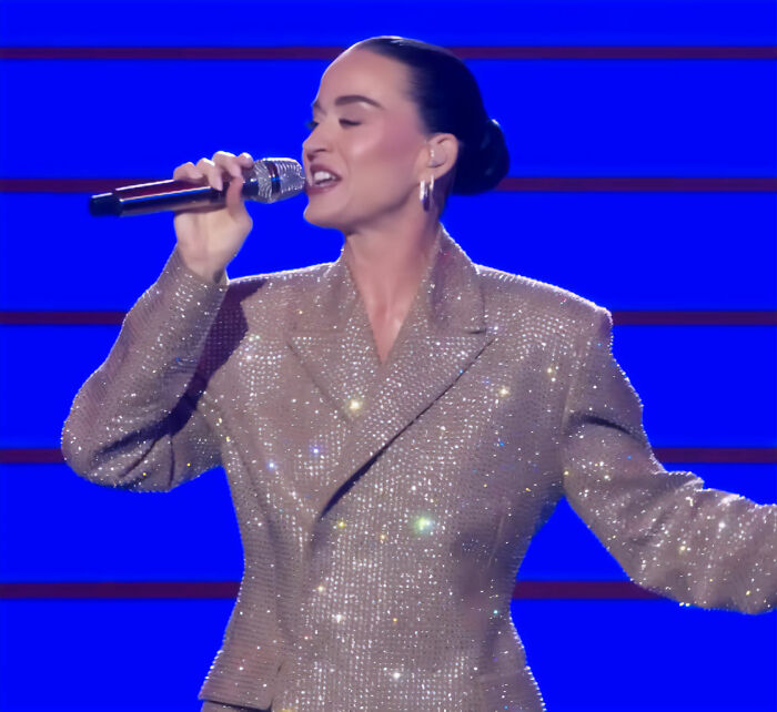 Katy Perry singing on stage in a sparkly jacket, her grim response to struggling fan sparking widespread backlash.