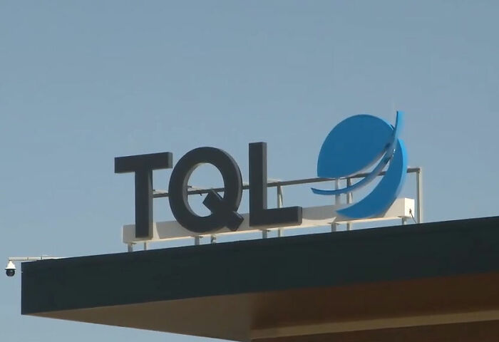 Placa de construção da empresa TQL contra céu claro, relacionada à indenização concedida à mãe após solicitação de trabalho em casa negada.