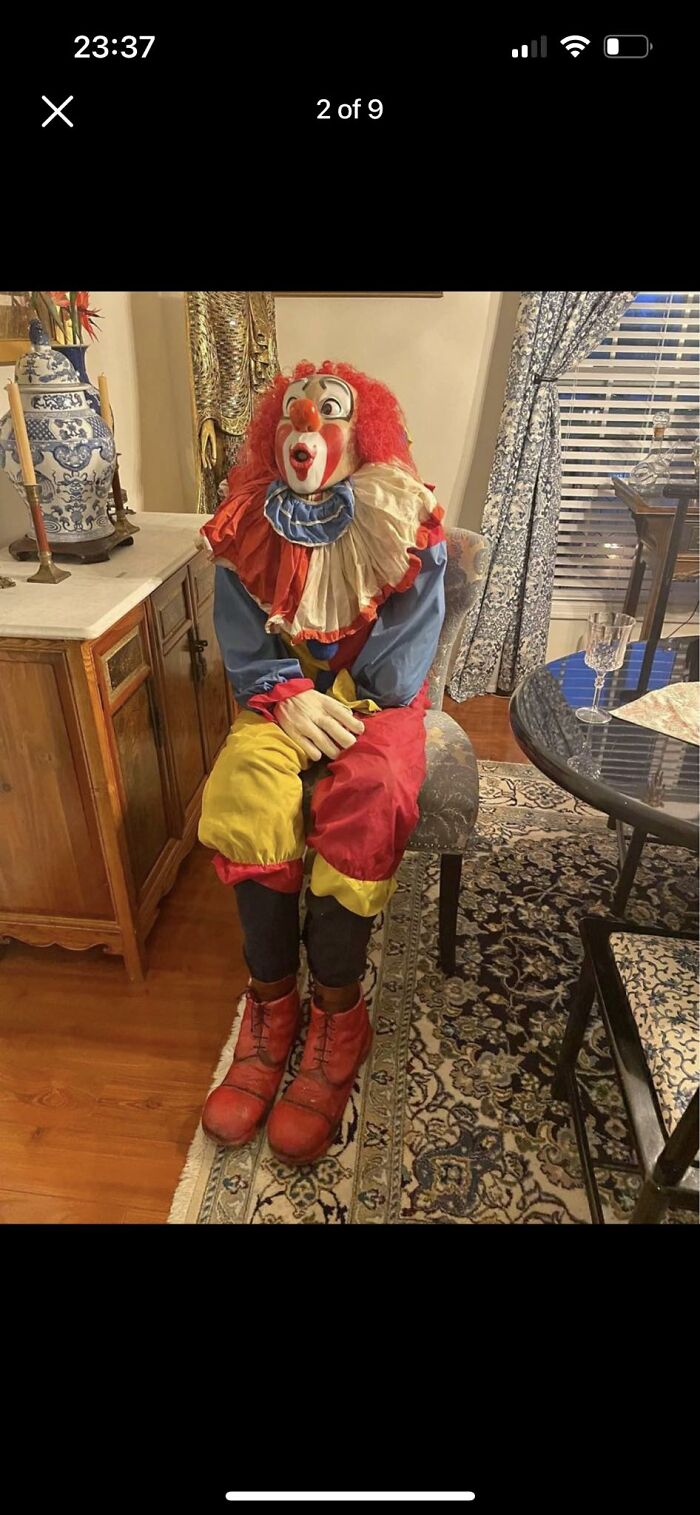 Clown figure in colorful costume sitting on a chair in a vintage-style living room, Facebook Marketplace unhinged pics.